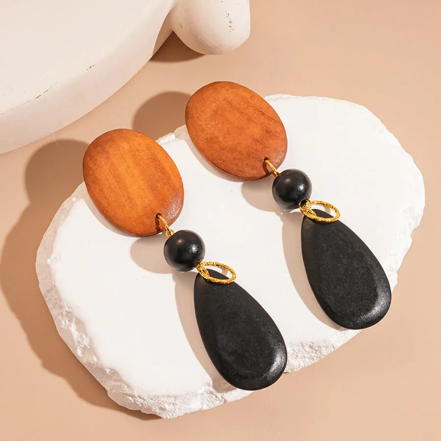 Close-up of handmade brown and black wooden ellipse earrings with silver needle fastenings on a textured background.