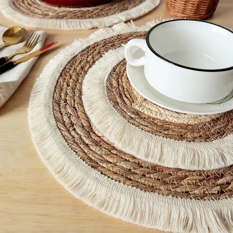 Round natural papyrus straw placemat with decorative tassel edge on a wooden table.