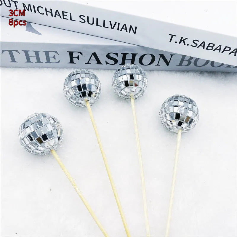 Glass disco ball cake decoration with a wooden stick inserted into a cake, showing reflective surface.
