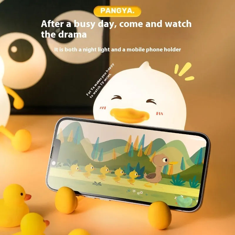 Chubby silicone and plastic night light on desk holding a mobile phone with soft LED glow.
