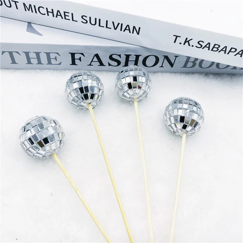 Glass disco ball cake decoration with a wooden stick inserted into a cake, showing reflective surface.