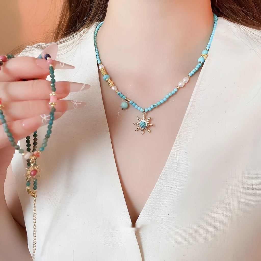 French royal style sun necklace with stone pendant and freshwater pearls on a gold and blue chain.