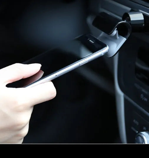Black 360-degree rotating gravity car phone holder mounted on a car dashboard, holding a mobile phone.