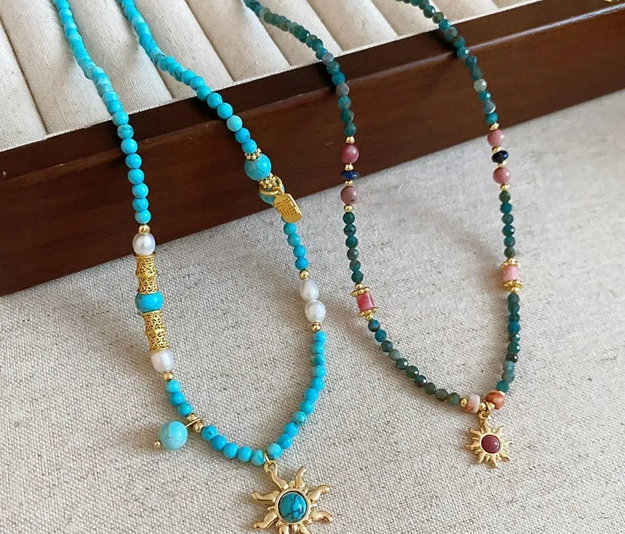 French royal style sun necklace with stone pendant and freshwater pearls on a gold and blue chain.