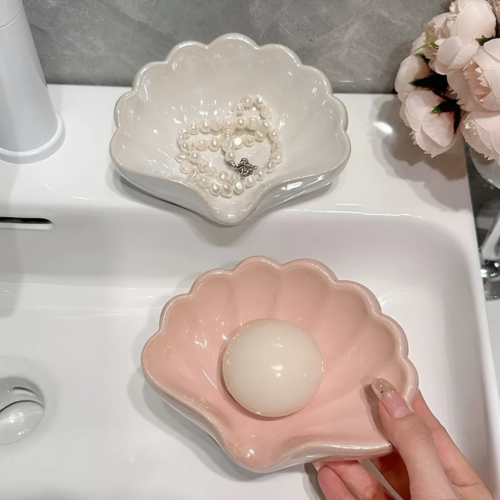 White plastic shell-shaped soap dish for bathroom countertop with soap bar on it.
