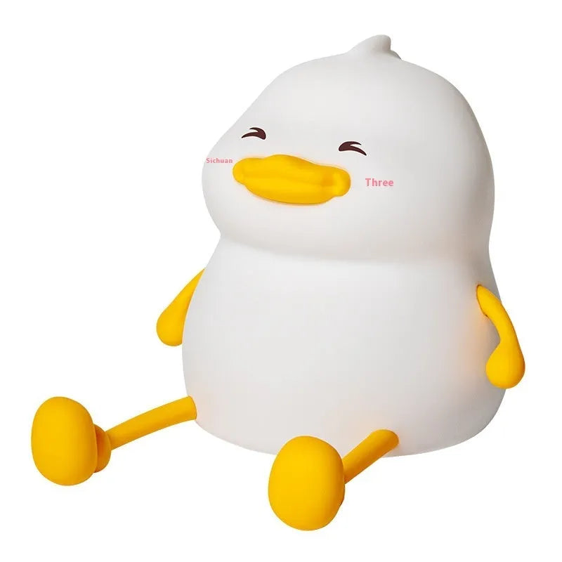 Chubby silicone and plastic night light on desk holding a mobile phone with soft LED glow.