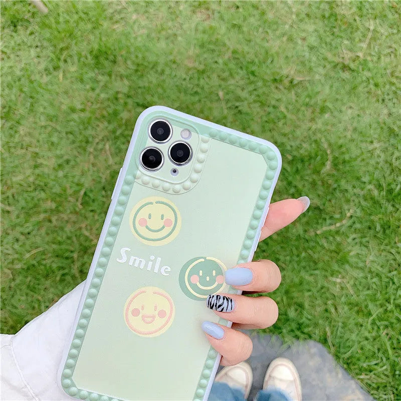 Green TPU iPhone case with geometric smiley face design and polka dot frame on a phone.
