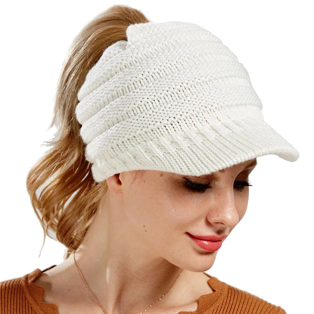 Woman wearing a light grey knitted beanie with a ponytail pulled through the back opening.