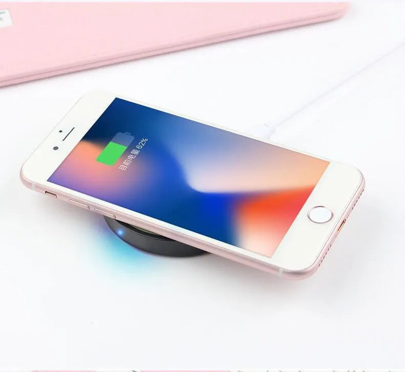 Slim square Qi wireless charging pad in one of six colours on a desk next to a mobile phone.