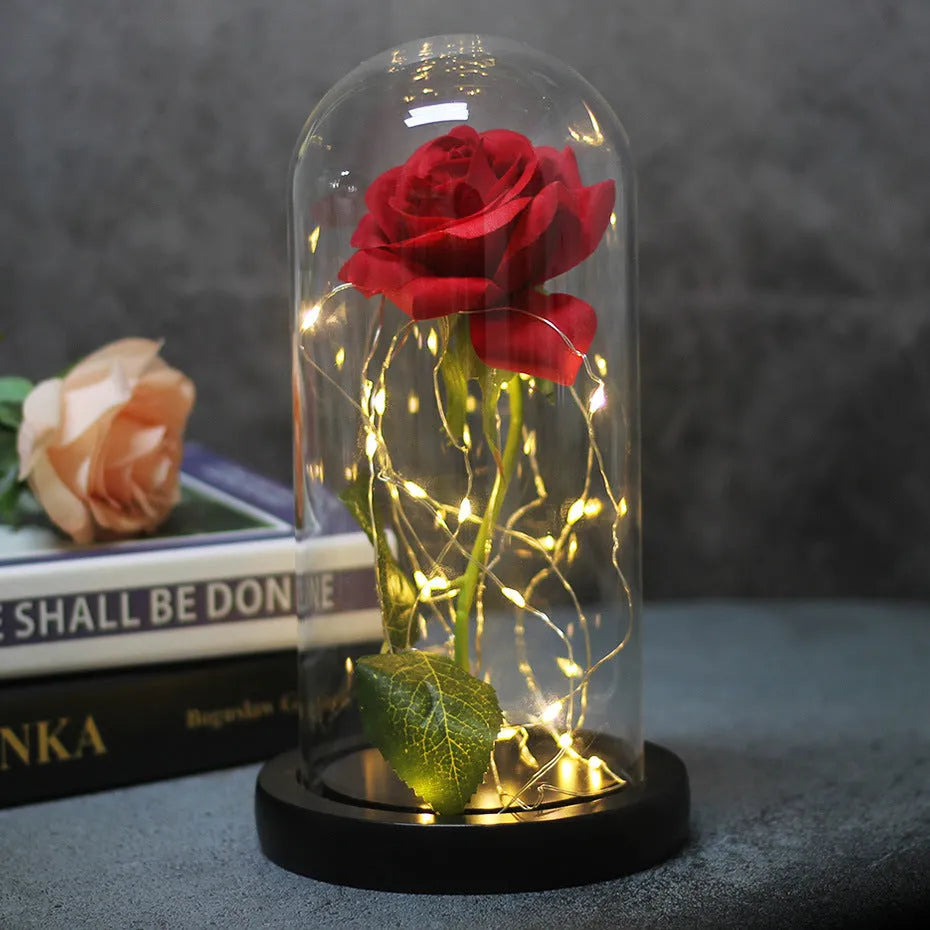 Artificial rose LED bouquet with glass shade and warm white light on a solid wood base.