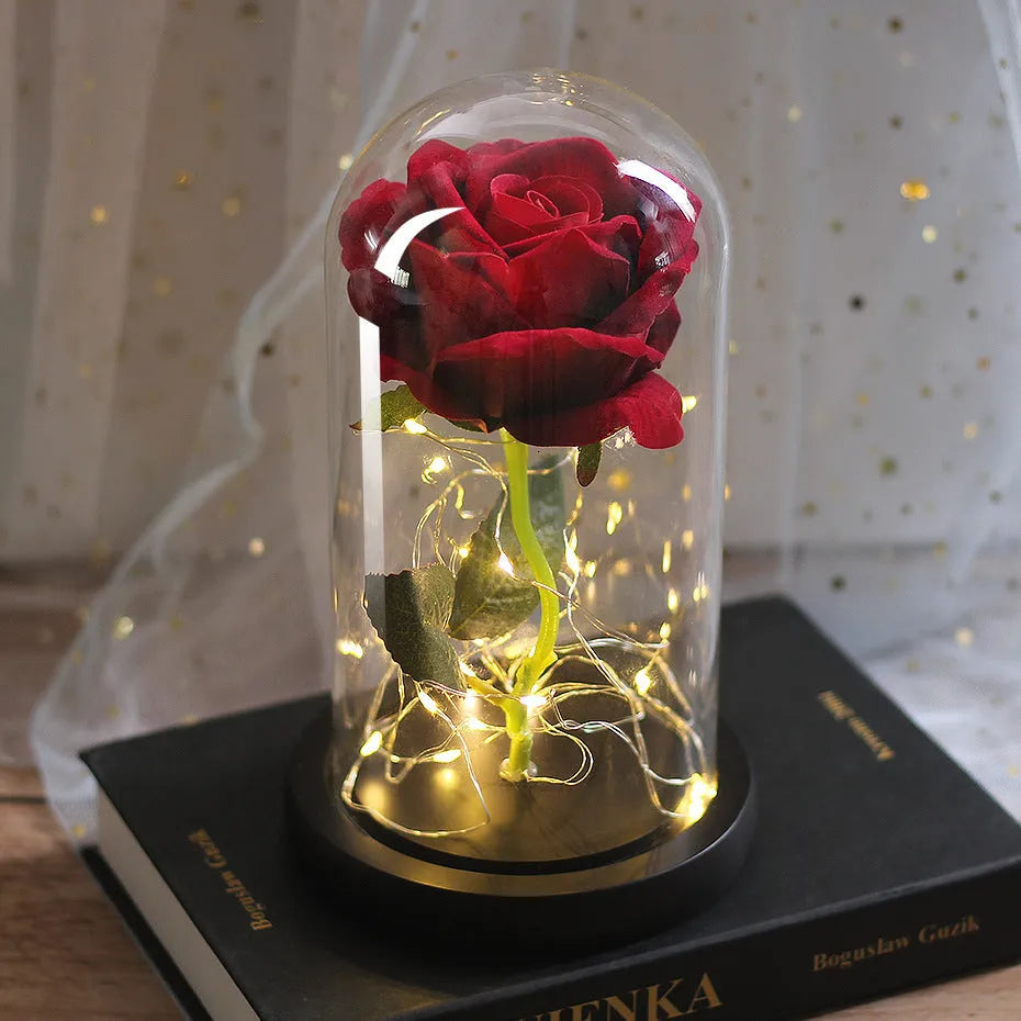 Artificial rose LED bouquet with glass shade and warm white light on a solid wood base.