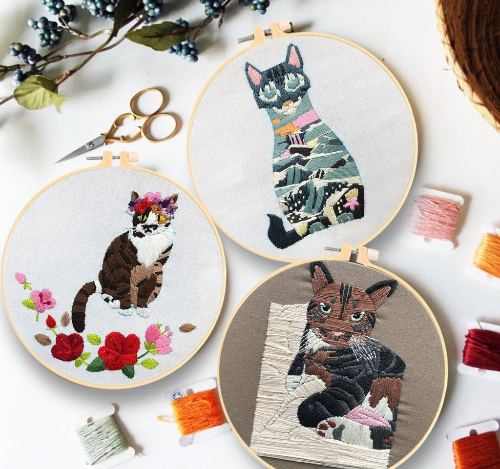 Cross stitch kit for 3D cat embroidery with hoop, fabric, and threads on a wooden table.