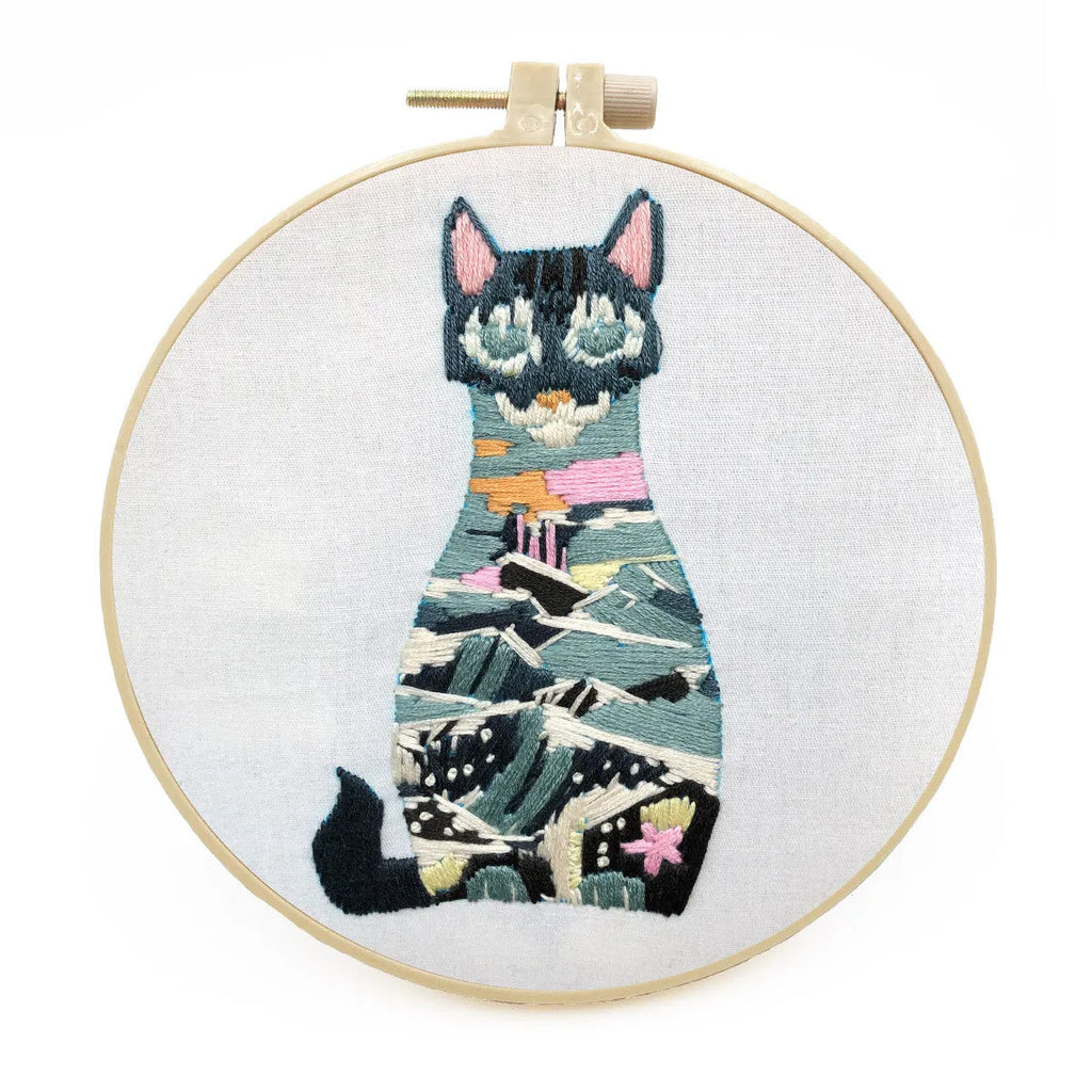 Cross stitch kit for 3D cat embroidery with hoop, fabric, and threads on a wooden table.