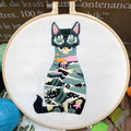 Cross stitch kit for 3D cat embroidery with hoop, fabric, and threads on a wooden table.