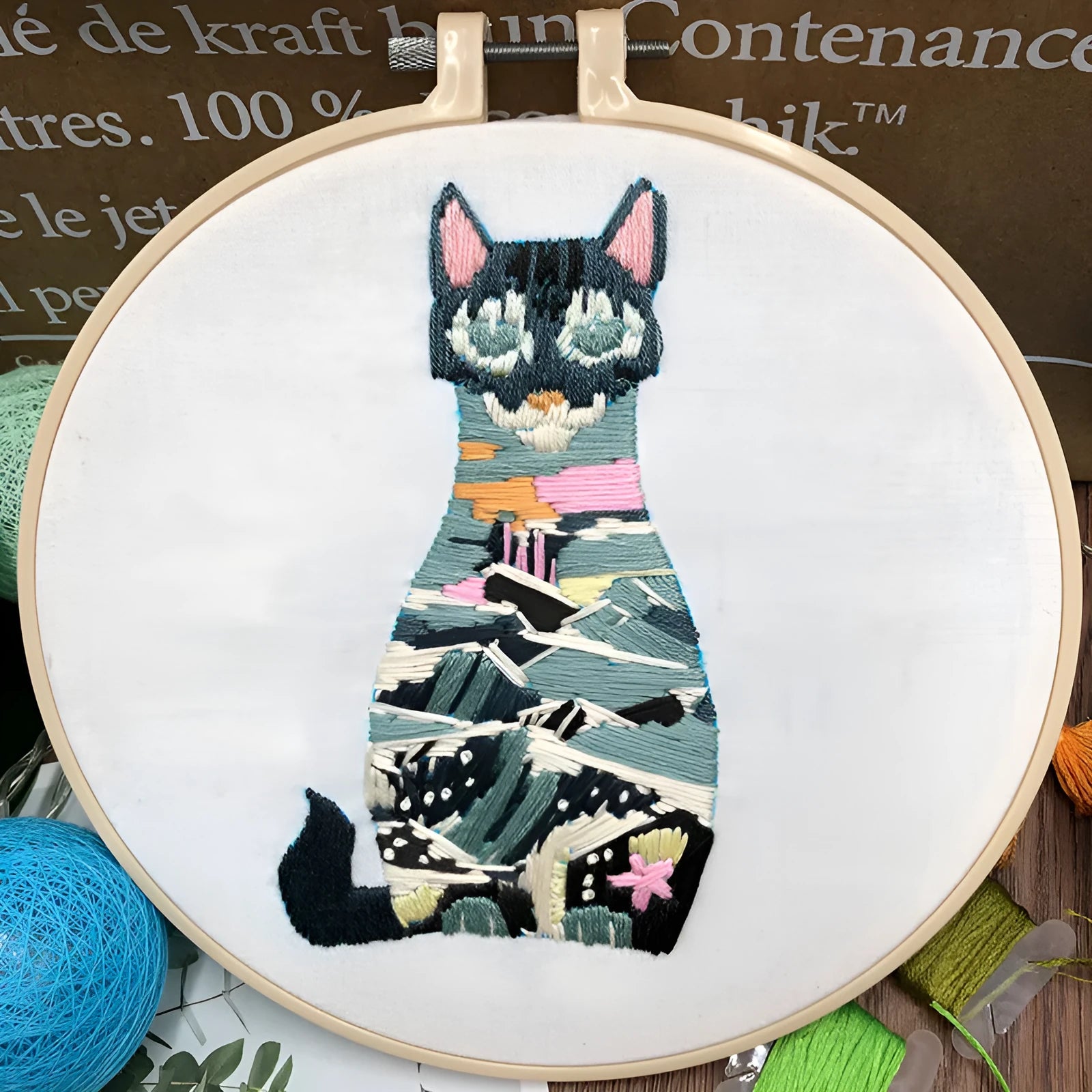 Cross stitch kit for 3D cat embroidery with hoop, fabric, and threads on a wooden table.