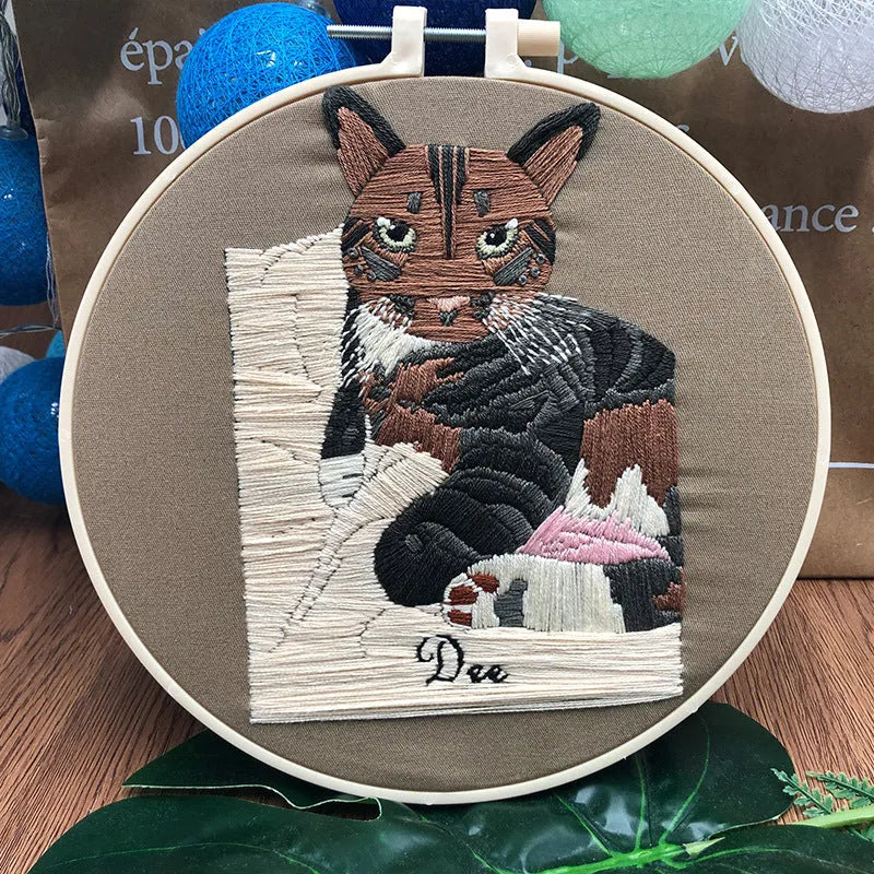 Cross stitch kit for 3D cat embroidery with hoop, fabric, and threads on a wooden table.