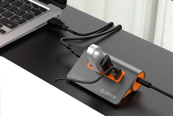 Dark grey aluminium USB-C hub with orange accents showing four USB 3.1 ports and detachable cable