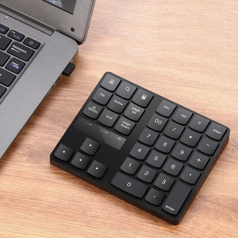 Black wireless 35-key numeric keyboard with USB receiver and charging cable on desk