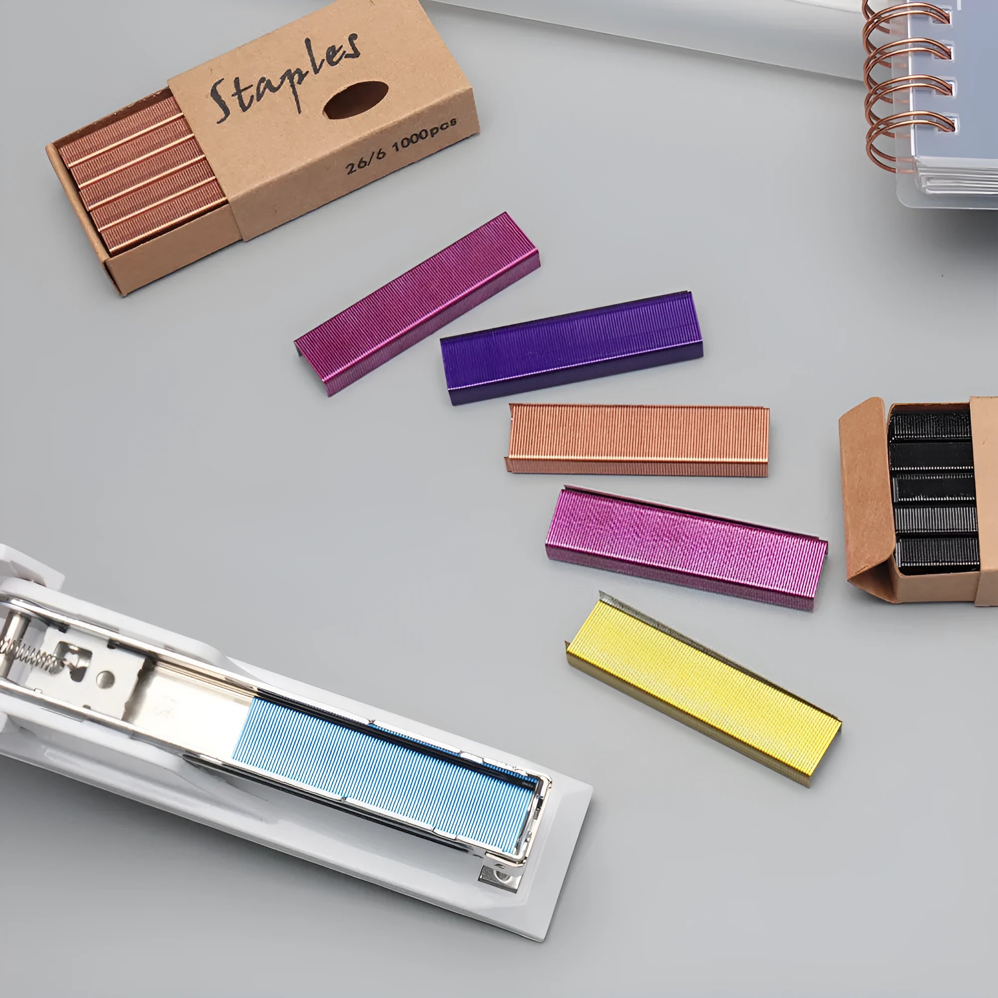 A box of 1000 metal office staples in rose gold, black, purple, and rose red colour options.