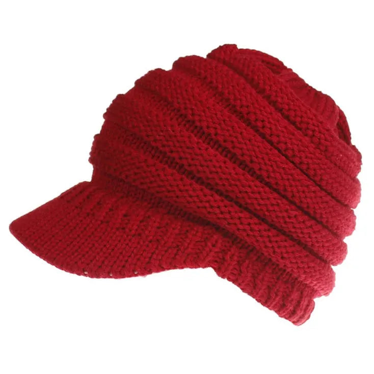 Woman wearing a light grey knitted beanie with a ponytail pulled through the back opening.