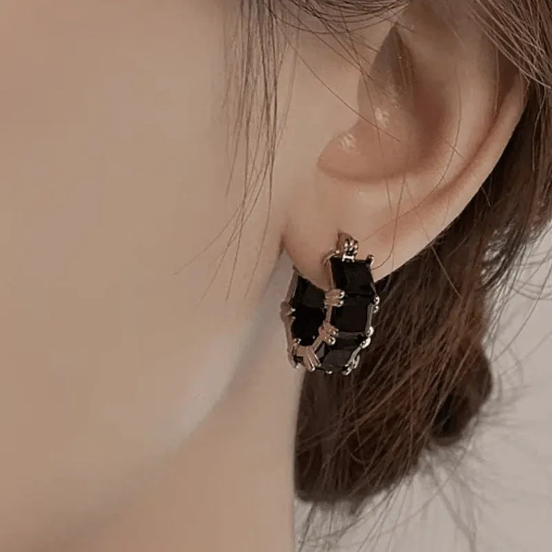 Geometric U-shaped gold earring with a round black zirconium stone on a copper base.