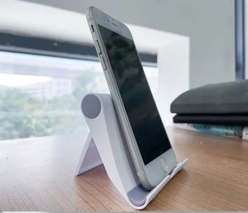 Black PE folding mobile phone stand holding a tablet at an angle on a wooden desk.