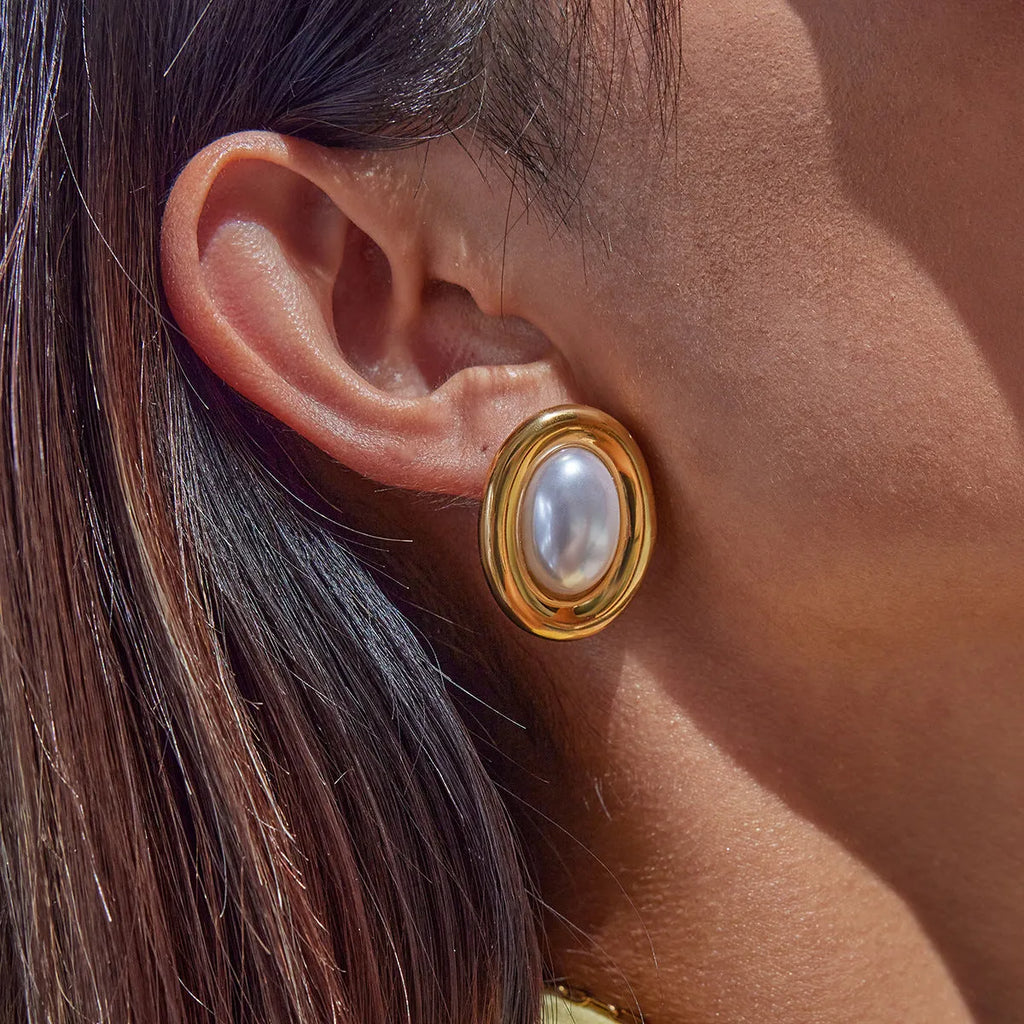 A pair of stainless steel post ear studs with small vintage-style pearl accents on a silver-tone background.