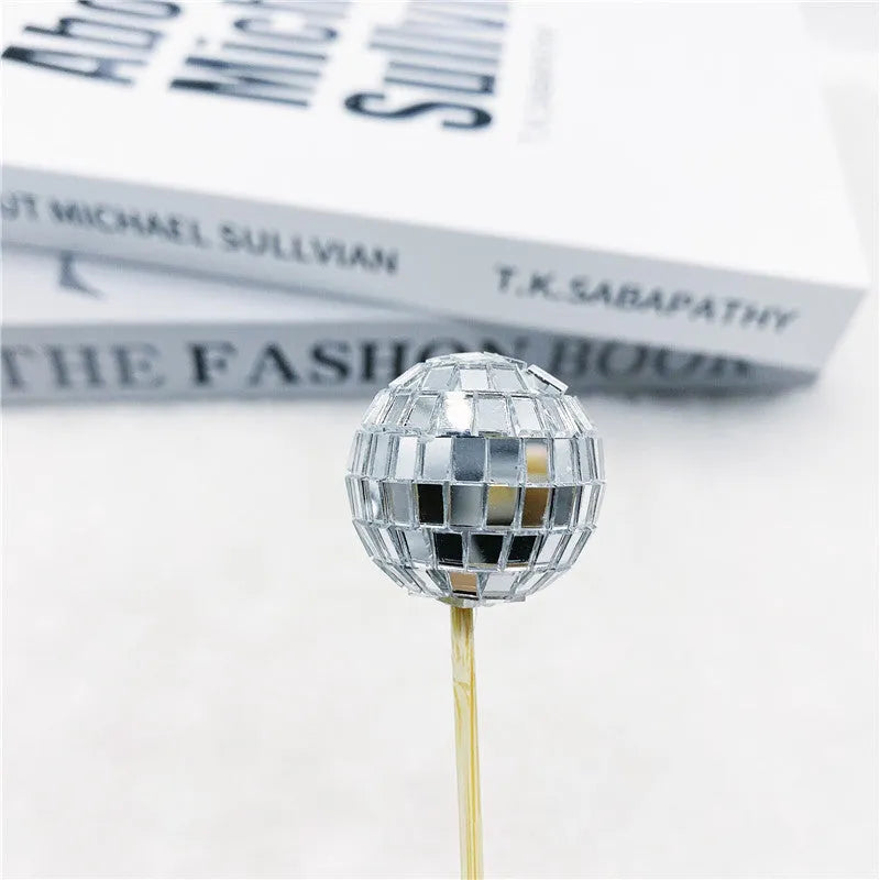 Glass disco ball cake decoration with a wooden stick inserted into a cake, showing reflective surface.