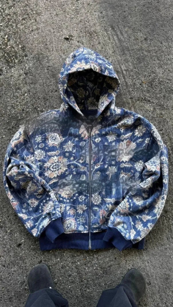 A man's loose fitting blue hooded zip-up coat with long sleeves on a hanger.