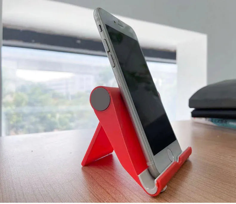 Black PE folding mobile phone stand holding a tablet at an angle on a wooden desk.