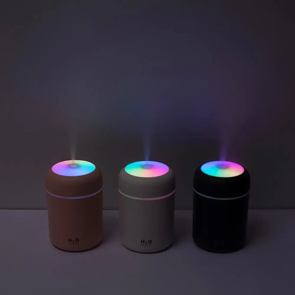 Pink USB desktop humidifier with LED lights next to a white mug on a desk