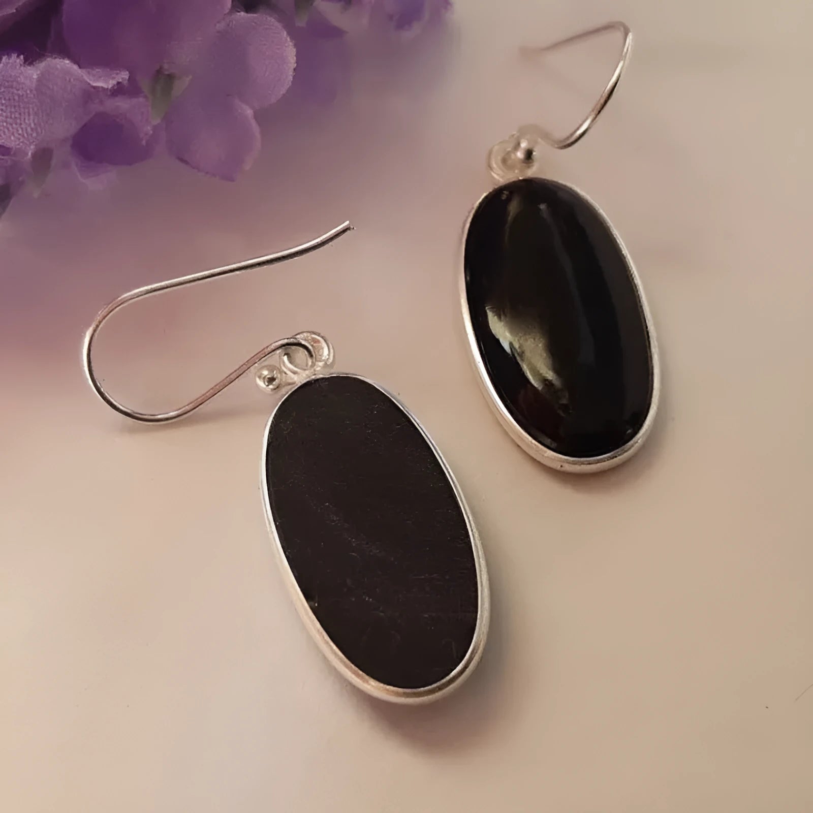Close-up of women's earrings with black agate oval pendant and silver electroplated geometrical alloy design.
