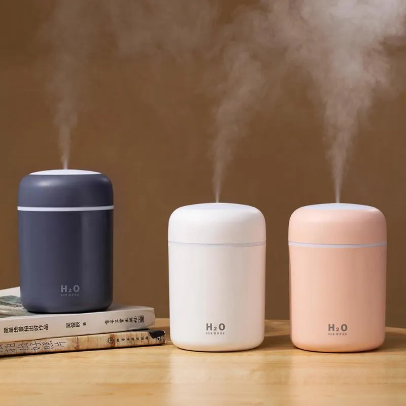 Pink USB desktop humidifier with LED lights next to a white mug on a desk