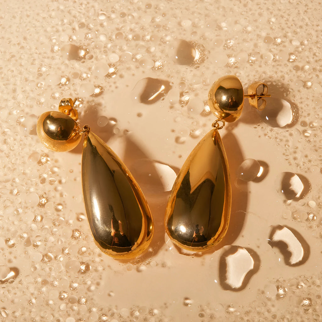 Gold-coloured stainless steel earrings featuring a geometric hemisphere shape with a dangling water drop pendant.