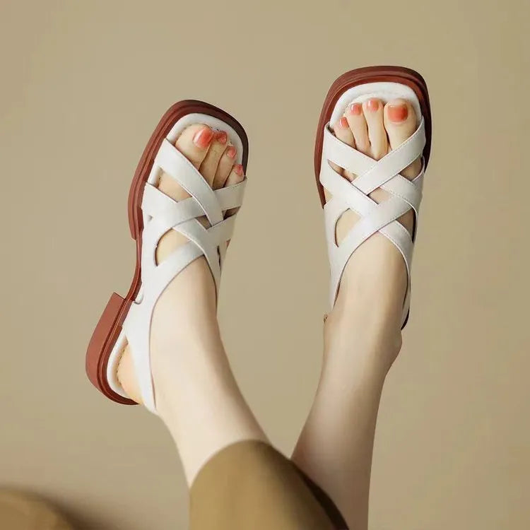 Women's glossy patent leather sandals with cross-belt straps, square toe, and a low block heel.