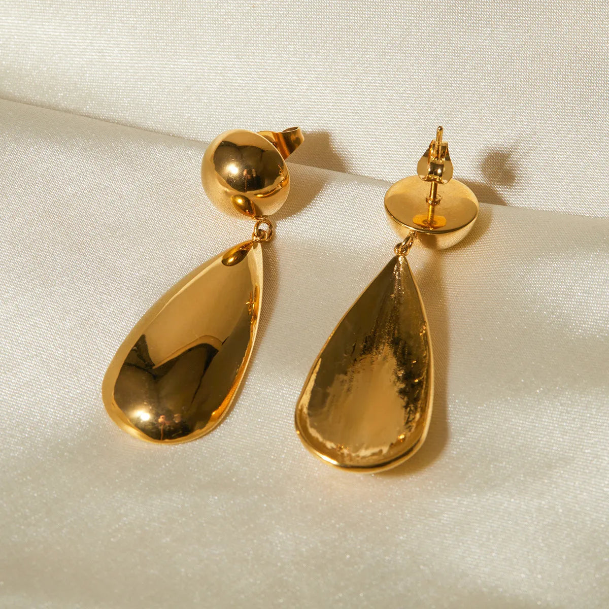 Gold-coloured stainless steel earrings featuring a geometric hemisphere shape with a dangling water drop pendant.
