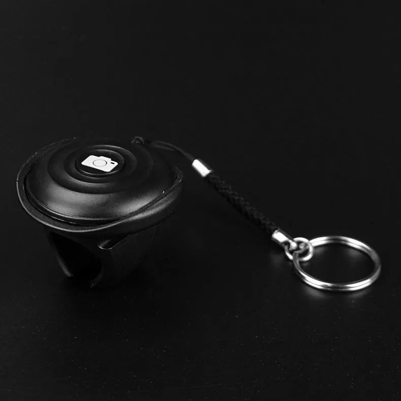 Black Bluetooth remote shutter release for smartphone camera on a white background.