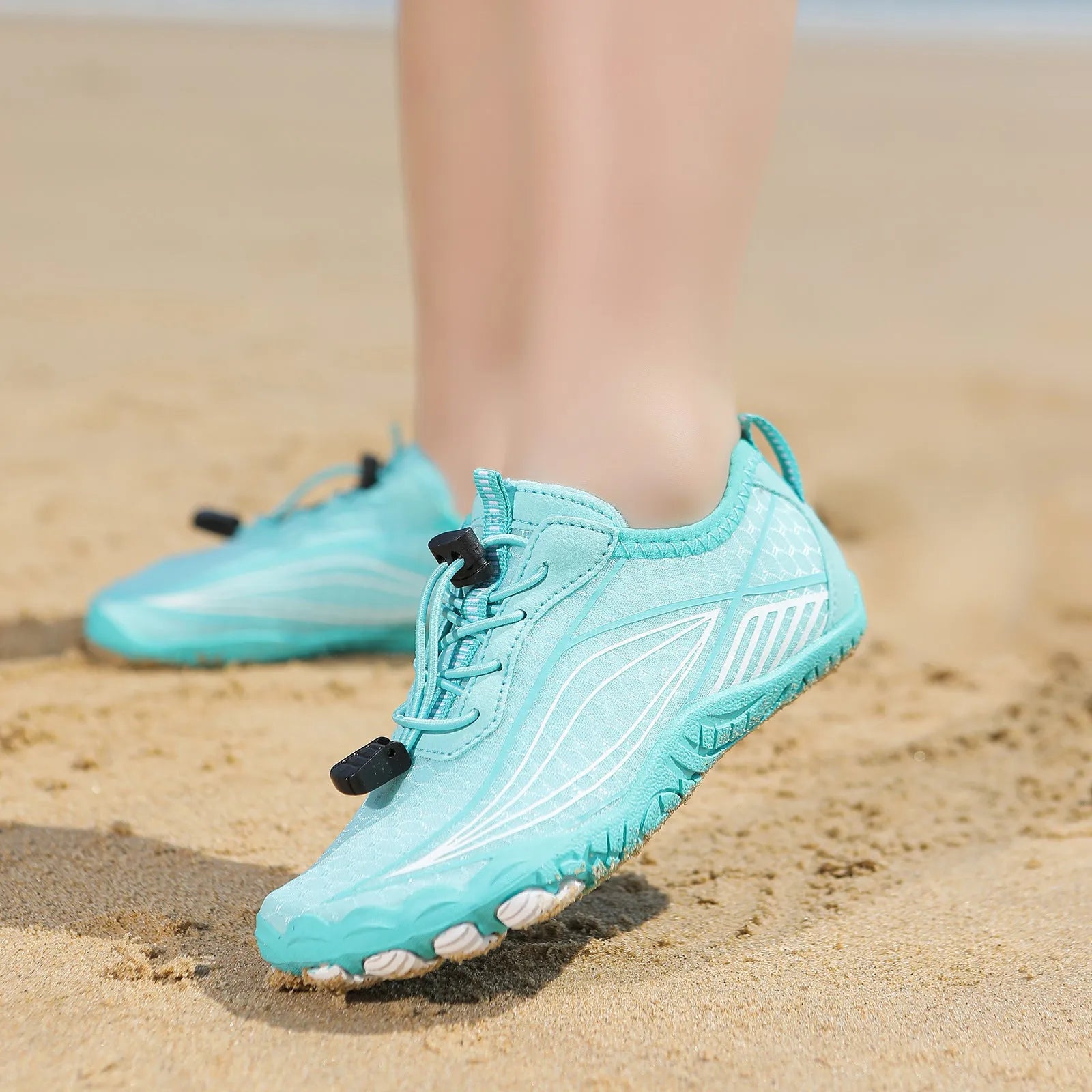 Children's elastic band wading shoes in grey with non-slip rubber sole, shown on a beach.