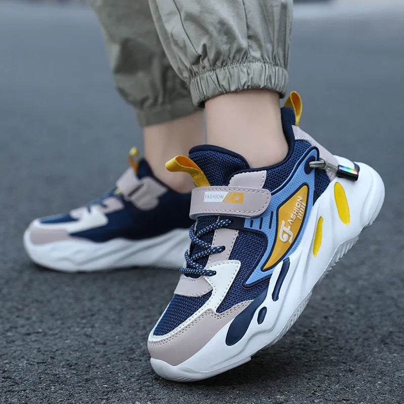 Boys' blue and black platform sports running shoes with Velcro strap on a hard ground surface.