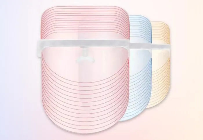 Transparent ABS LED light therapy face mask with red blue yellow lights and USB cable on a flat surface