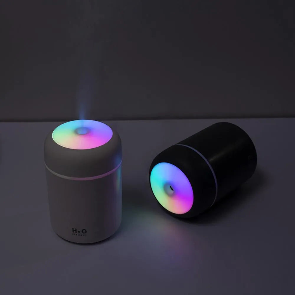 Pink USB desktop humidifier with LED lights next to a white mug on a desk