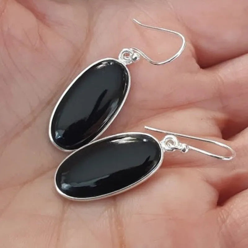 Close-up of women's earrings with black agate oval pendant and silver electroplated geometrical alloy design.