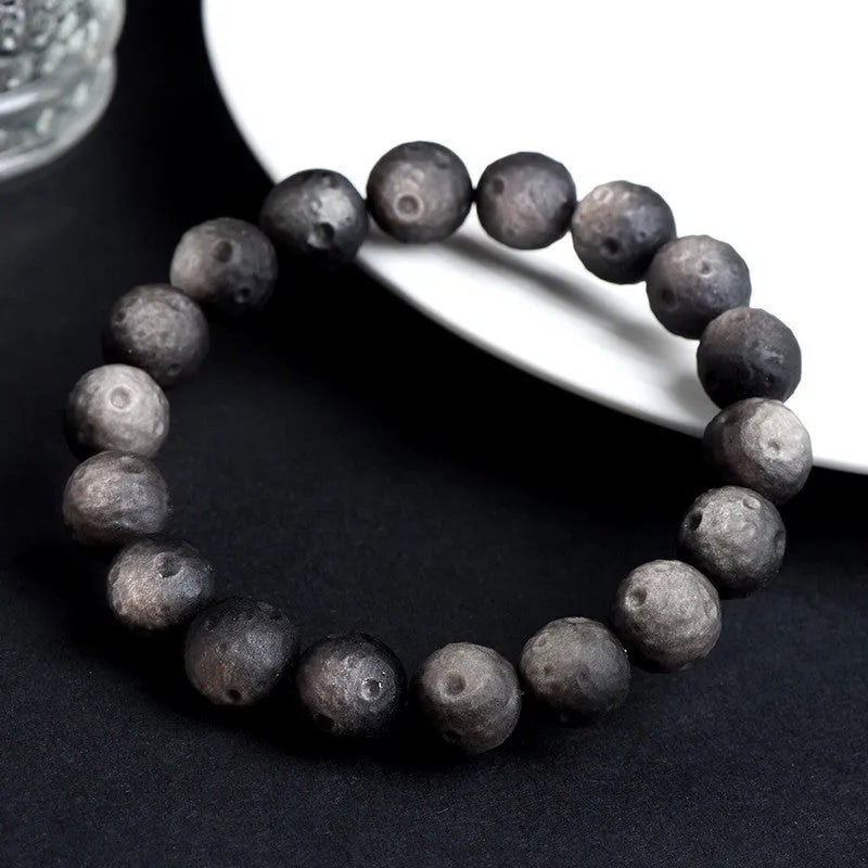 Natural obsidian crater ball bracelet showing polished spherical beads in silver stone meteorite colour with visible mineral texture