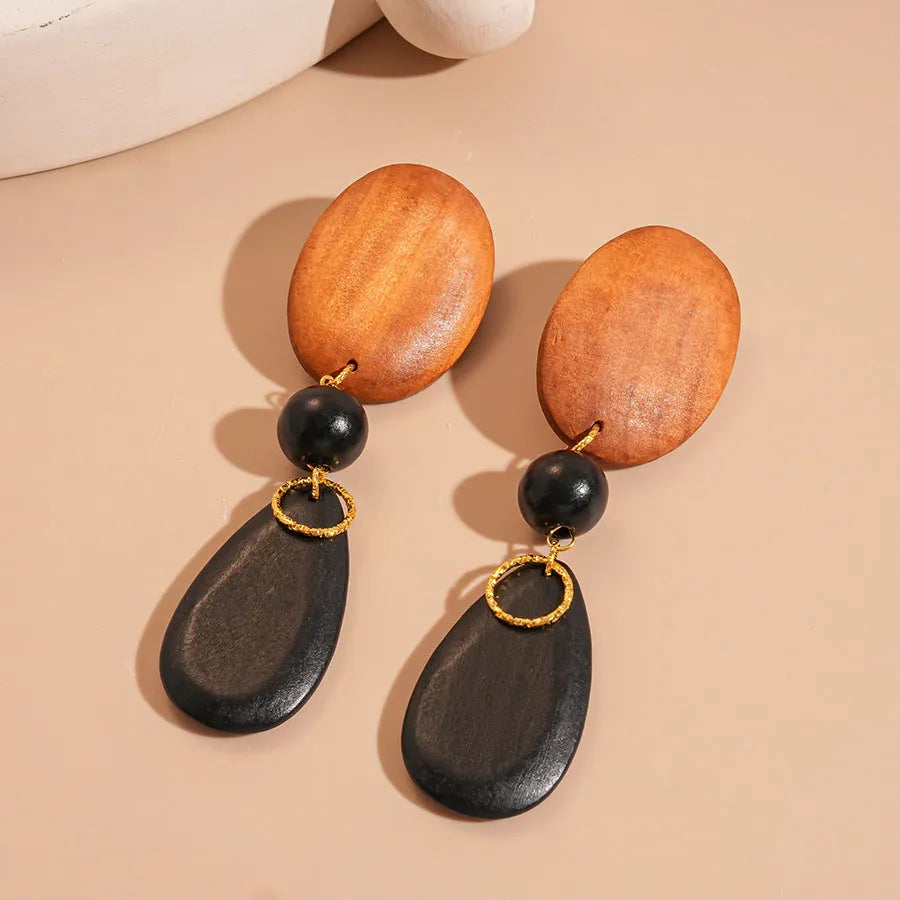 Close-up of handmade brown and black wooden ellipse earrings with silver needle fastenings on a textured background.