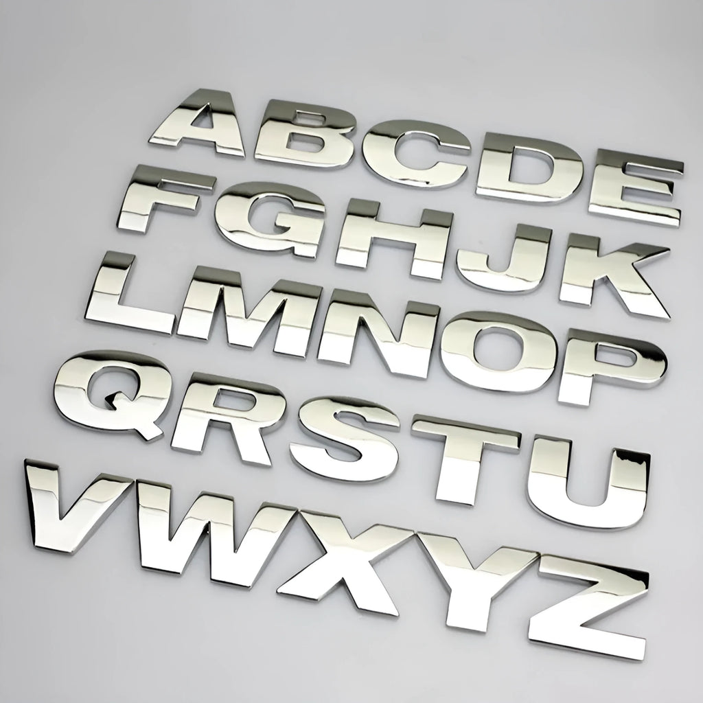 Close-up of a silver metal 3D letter 'A' car sticker with adhesive backing, shown next to a black version.
