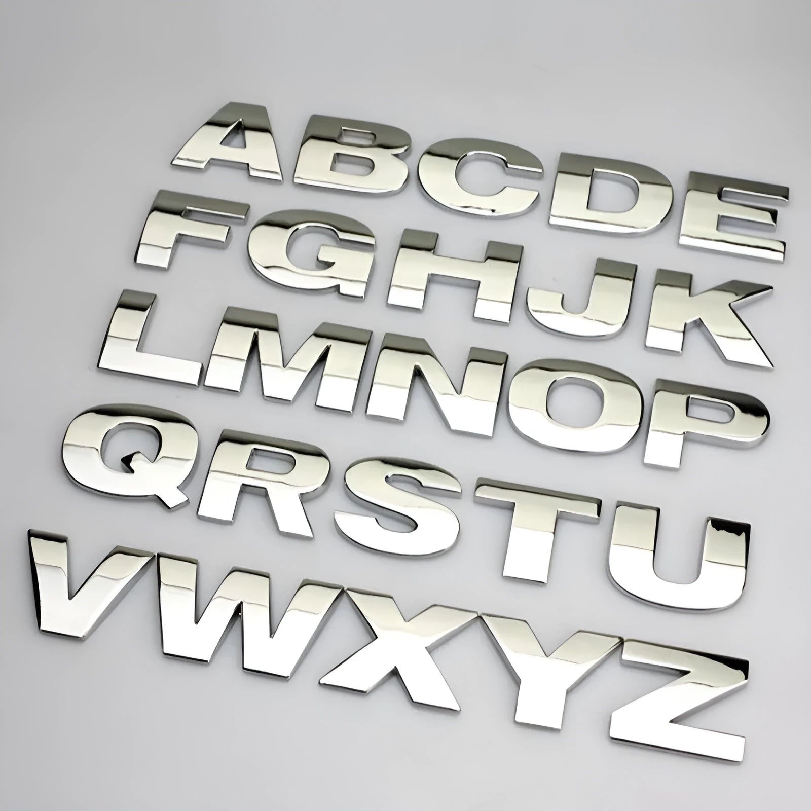Close-up of a silver metal 3D letter 'A' car sticker with adhesive backing, shown next to a black version.