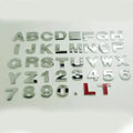 Close-up of a silver metal 3D letter 'A' car sticker with adhesive backing, shown next to a black version.