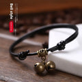 Black nylon rope dog collar with a brass bell on a wooden surface.