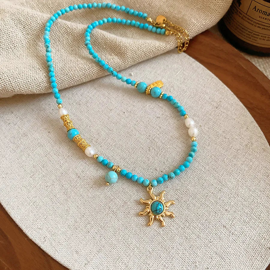 French royal style sun necklace with stone pendant and freshwater pearls on a gold and blue chain.