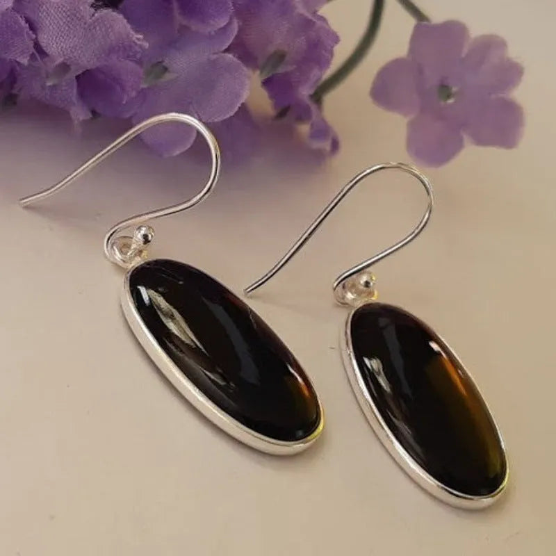 Close-up of women's earrings with black agate oval pendant and silver electroplated geometrical alloy design.
